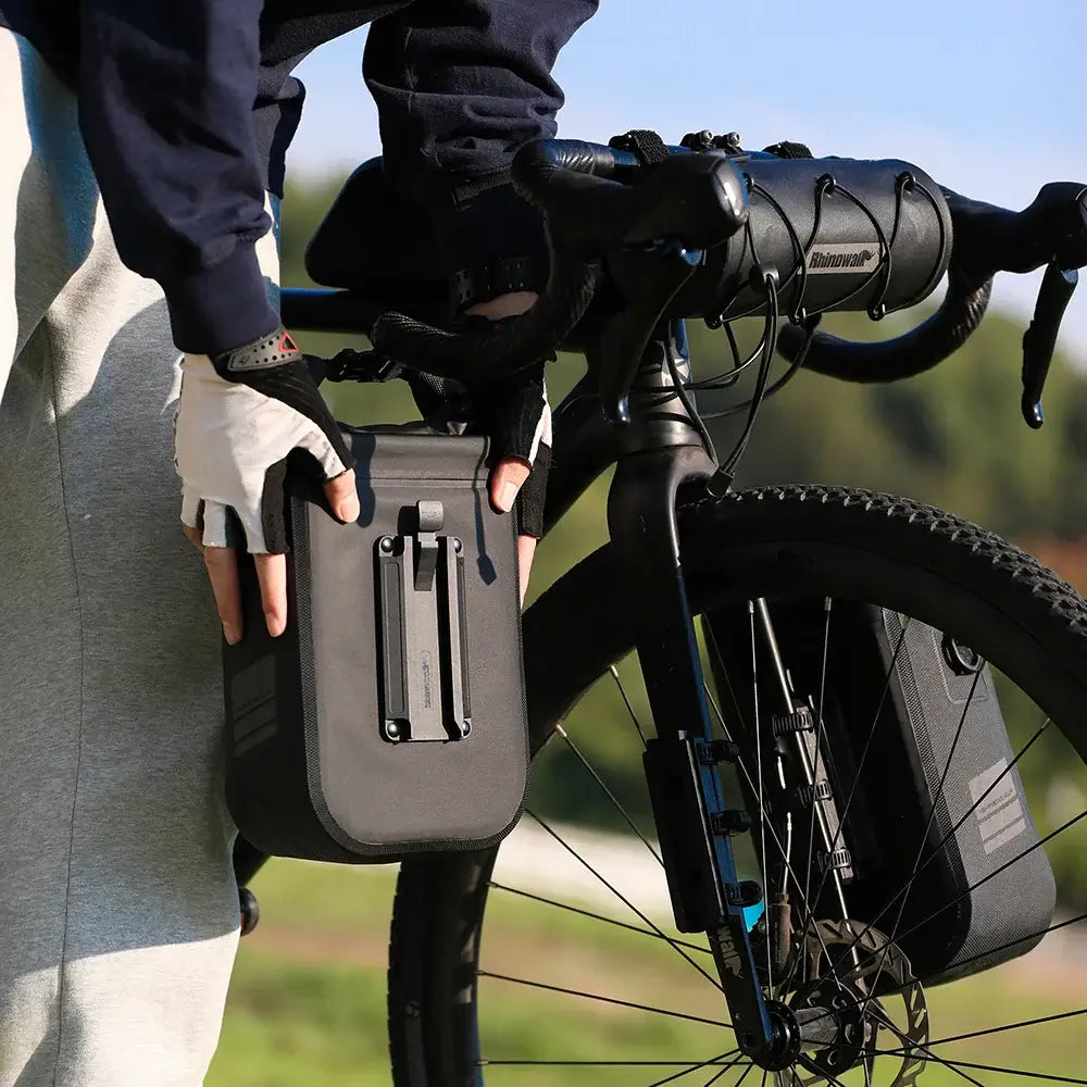 Person attaching a Rhinowalk waterproof bike bag to a bicycle fork during a cycling adventure.
